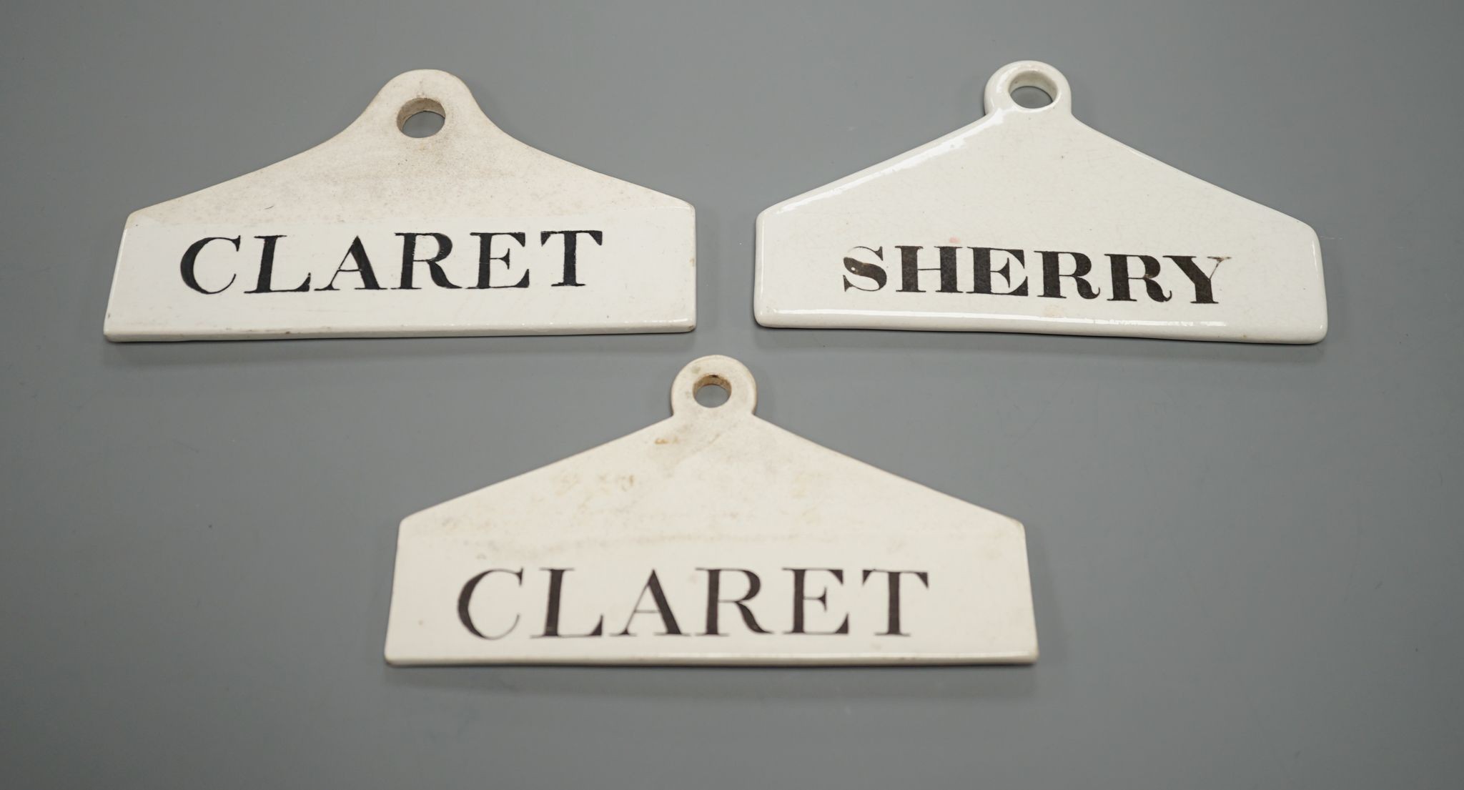 Three late 18th century creamware cellar labels, two claret stamped Wedgwood and one sherry, unmarked, 14 cms wide.